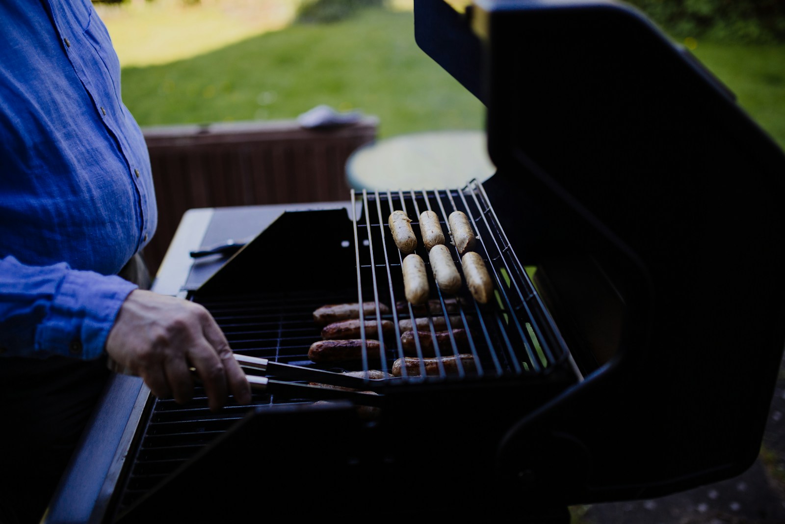 Eine Person grillt mehrere Bratwürste im Freien