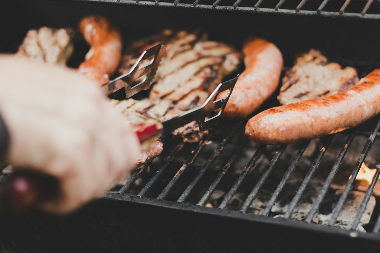 Person wendet Bratwürste und Fleisch auf dem Grill